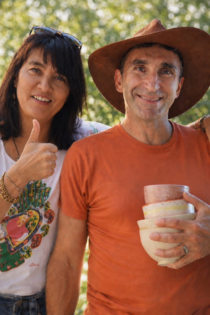 Pat et Jacques, hôtes de L’Arbre du Voyageur, souriants en extérieur avec des bols en céramique.